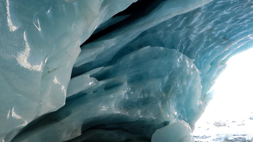 Intérieur d'une grotte de glacier montrant des formations de glace bleue et translucide, avec des ombres et reflets de lumière.