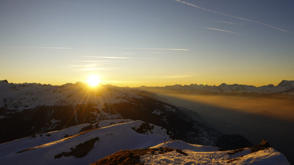 Coucher de soleil sur les montagnes enneigées, avec une vue panoramique des sommets alpins.